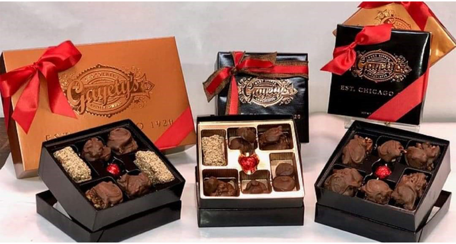 boxes of candy wrapped in a gold box with red ribbon and some boxes open with assorted chocolates