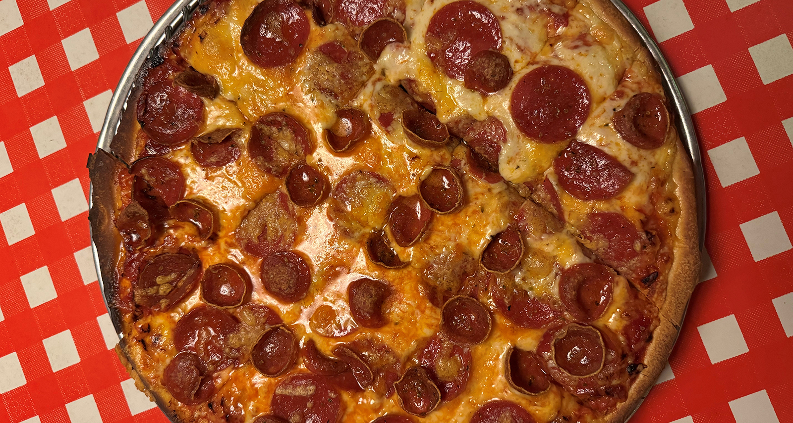 round pizza with crispy pepperoni on top with cheese on a red checkered background